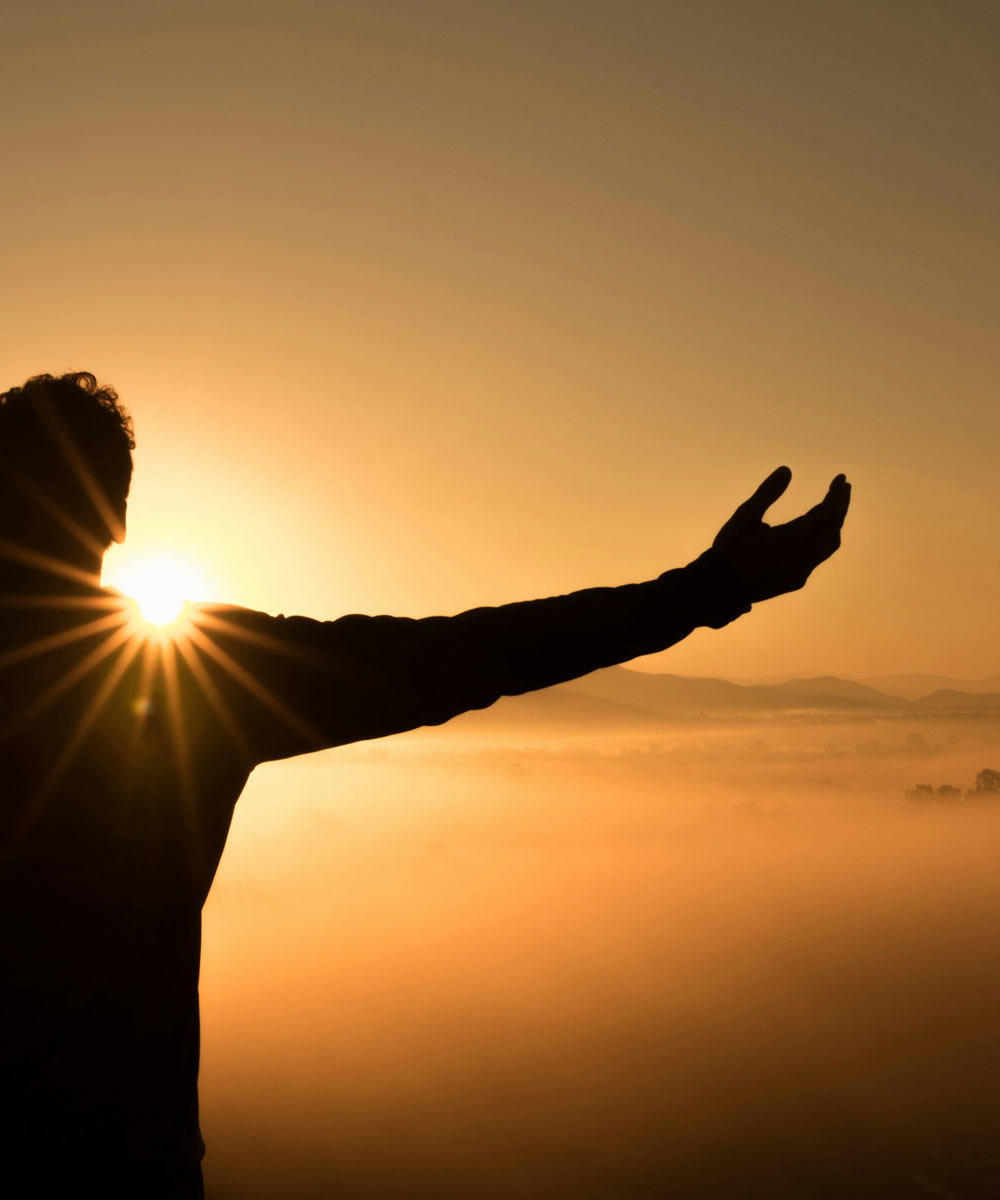 Person raising a hand in prayer at sunrise